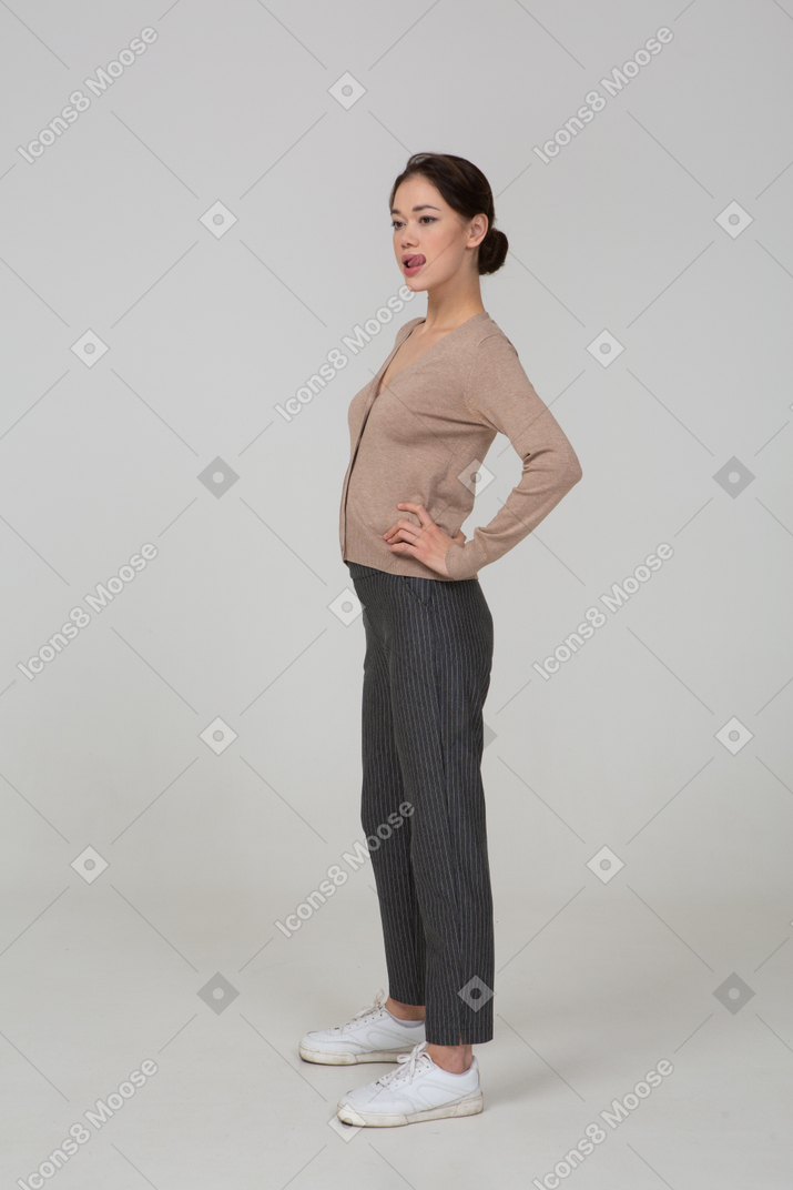 Three-quarter view of a young lady in pullover and pants putting hands on hips and showing tongue