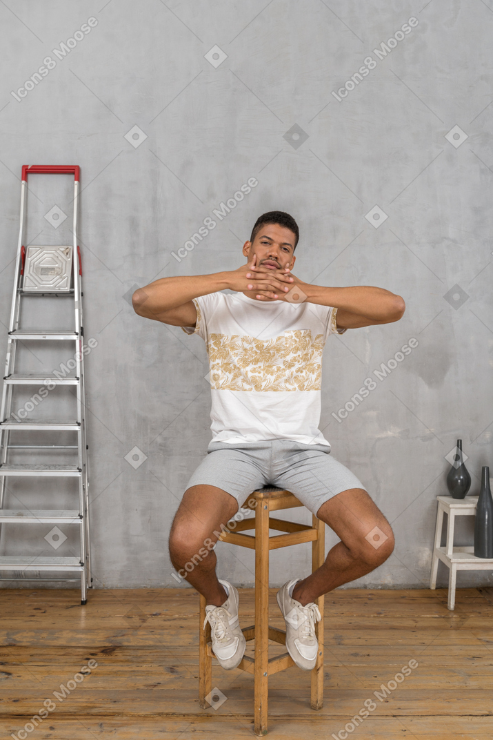 Vue de face du jeune homme assis sur une chaise avec les doigts entrelacés