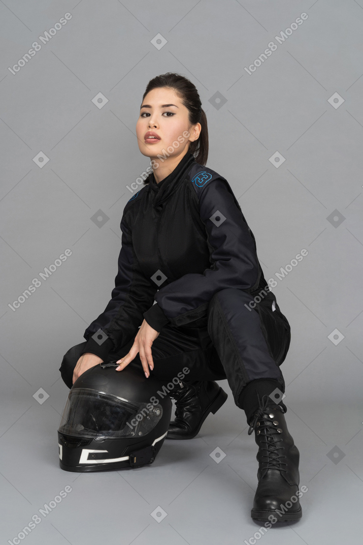 Motociclista feminino atraente, agachando-se com um capacete