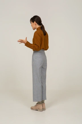 Three-quarter back view of a young gesticulating asian female in breeches and blouse