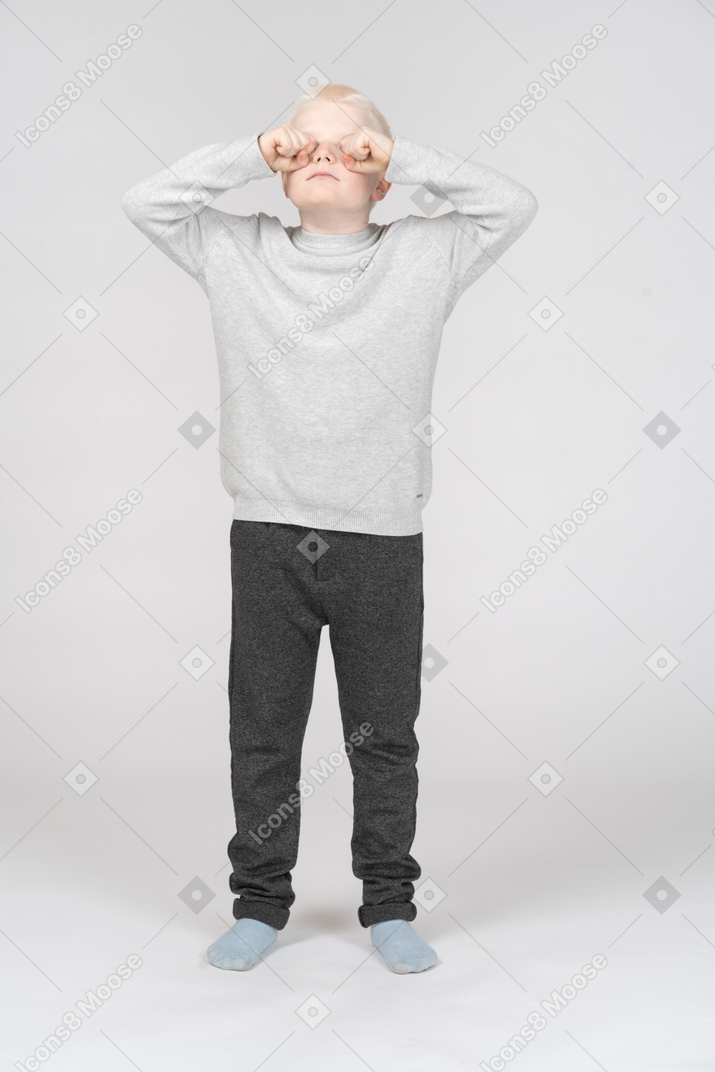 Front view of a boy rubbing his eyes with fists