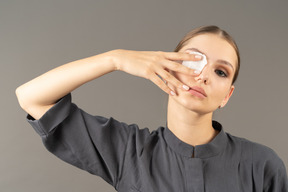 Front view of a young woman in a jumpsuit removing eye make-up