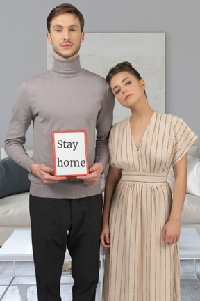 A man and woman holding a sign that says stay home