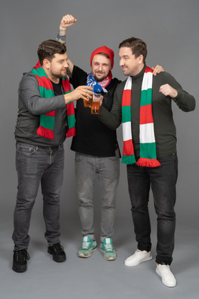 Vista frontal de tres aficionados al fútbol masculino celebrando la victoria.