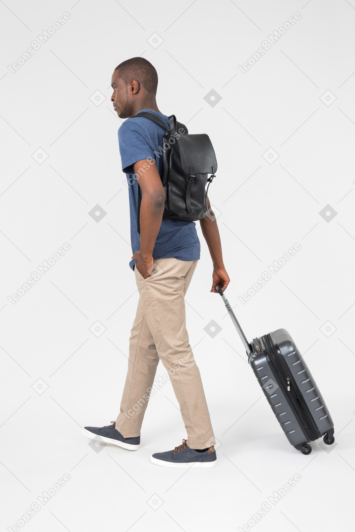 A man with a backpack pulling a suitcase