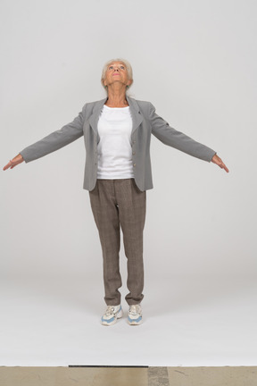 Front view of an old lady in suit standing on toes and outspreading arms