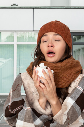 Young woman in a hat and scarf sneezing