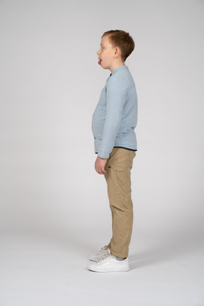 Vista lateral de um menino bonito em roupas casuais, mostrando a língua