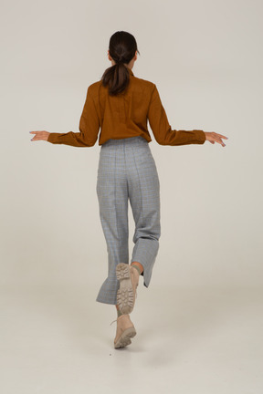 Back view of a jumping young asian female in breeches and blouse outspreading her hands