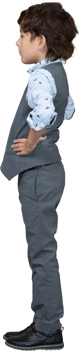 Vue latérale d'un garçon en costume posant avec les mains sur les hanches