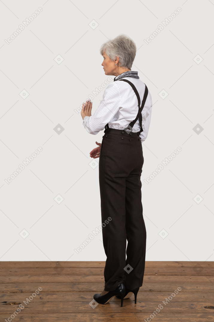 Three-quarter back view of a gesticulating unwilling old lady in office clothing