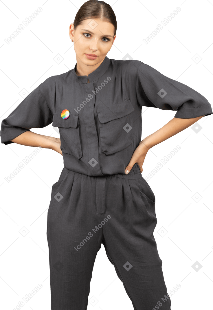 Front view of a young woman in a jumpsuit with lgbt pin putting hands on waist