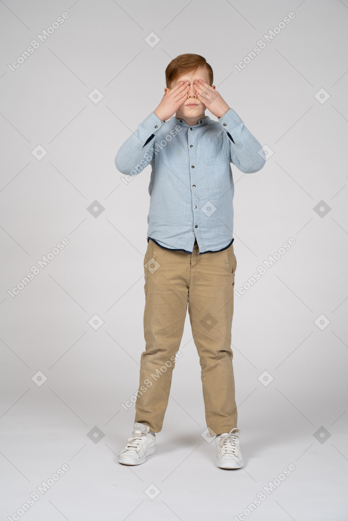 Vista frontal de un niño que cubre los ojos con las manos