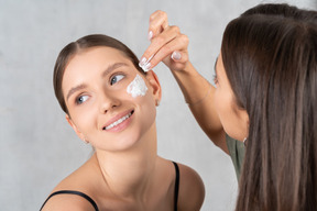 Mujer aplicando crema en la cara de otra mujer