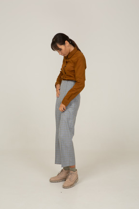 Вид сбоку молодой азиатской женщины в бриджах и блузке, кладя руки в карманы