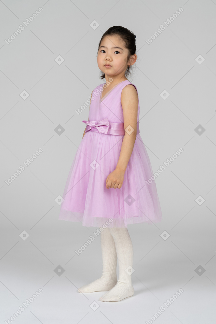 Милая маленькая девочка в розовом платье смотрит в камеру