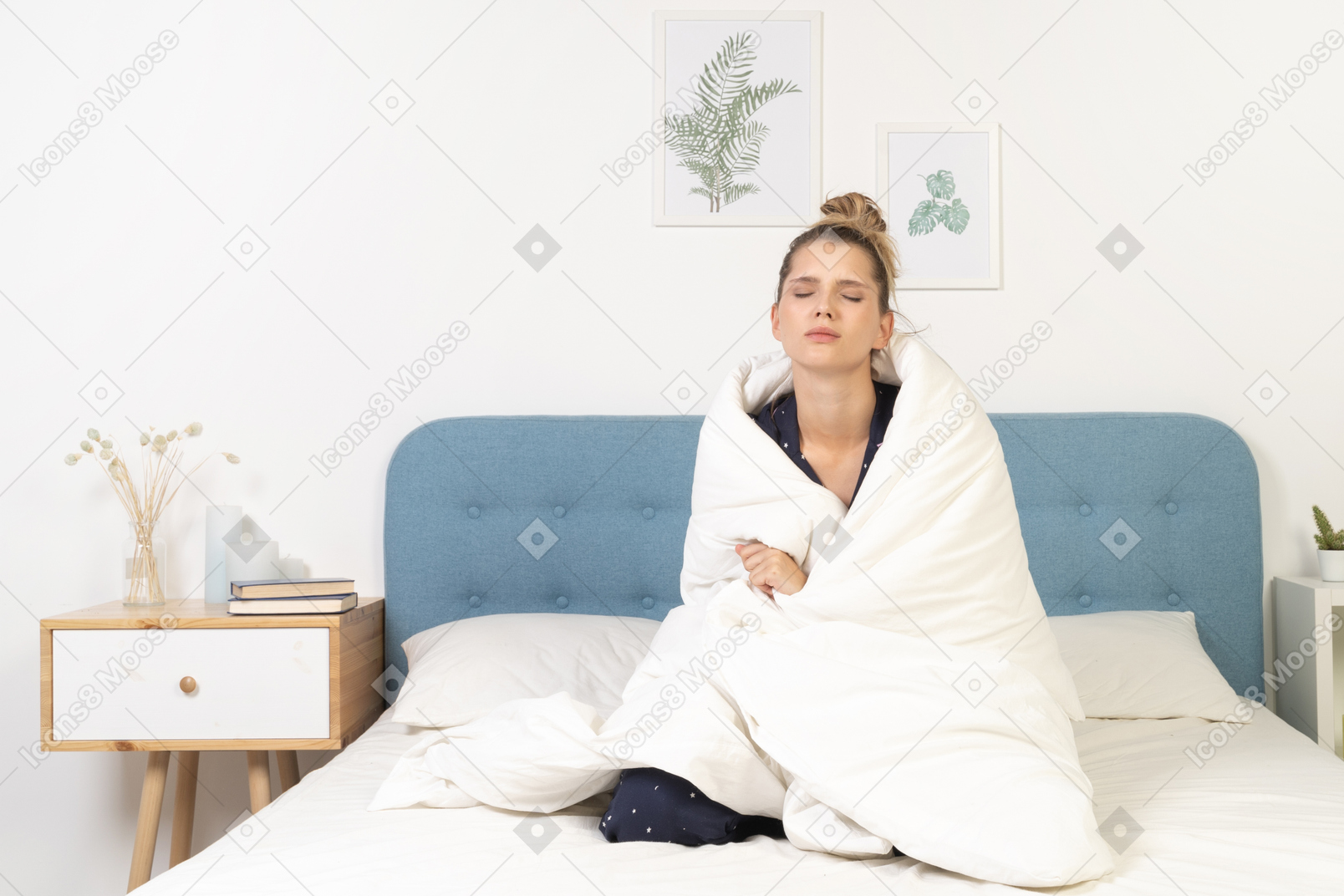 Front view of a tired young woman in pajamas wrapped in blanket staying in bed