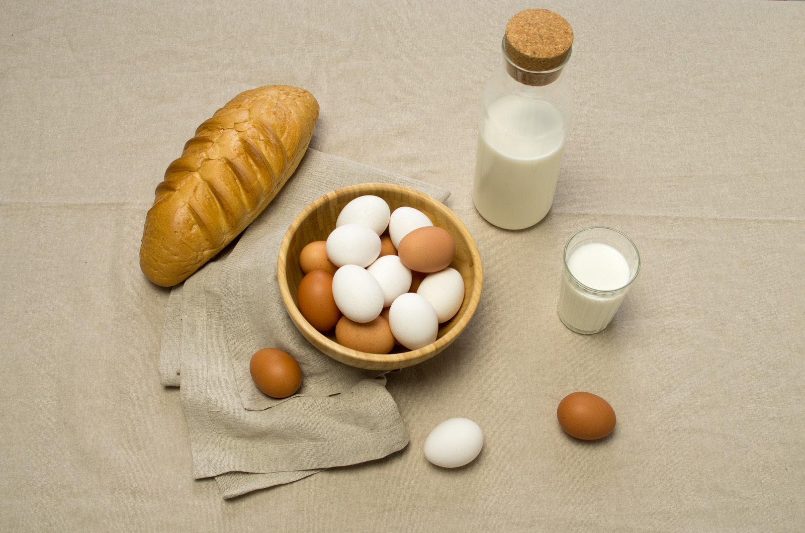 Chicken eggs, some milk and a loaf of bread on a gray tablecloth