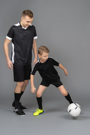 In voller länge von einem jungen mann, der einem kleinen jungen beibringt, wie man fußball spielt