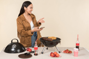 Lachende junge asiatische frau, die ein foto des grills macht