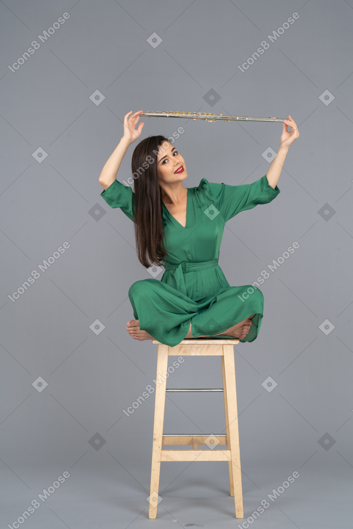 De cuerpo entero de una señorita sosteniendo su clarinete sobre la cabeza mientras está sentado en una silla de madera