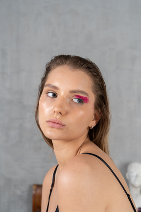 Portrait of a young woman with bold eye make-up looking behind her