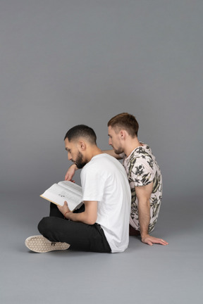 Side view of two young men sitting on the floor and reading