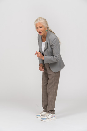 Vista lateral de uma senhora idosa de terno se abaixando e explicando algo