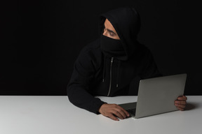 黑客人坐在桌前和在黑暗中的笔记本电脑上工作