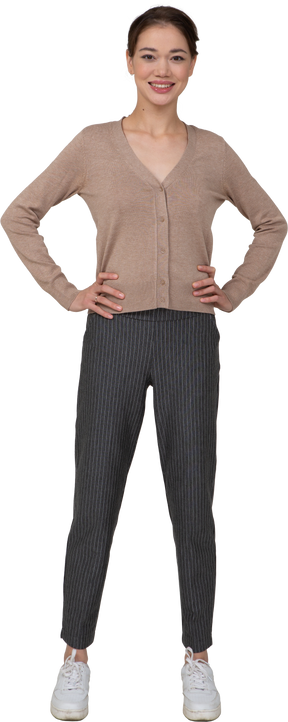 Vista frontale di una donna sorridente in pullover e pantaloni che mette le mani sui fianchi