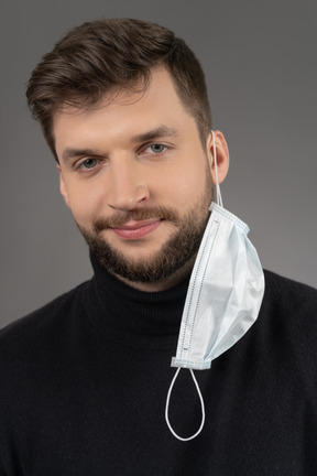 Homme caucasien souriant avec un masque respiratoire suspendu à une oreille