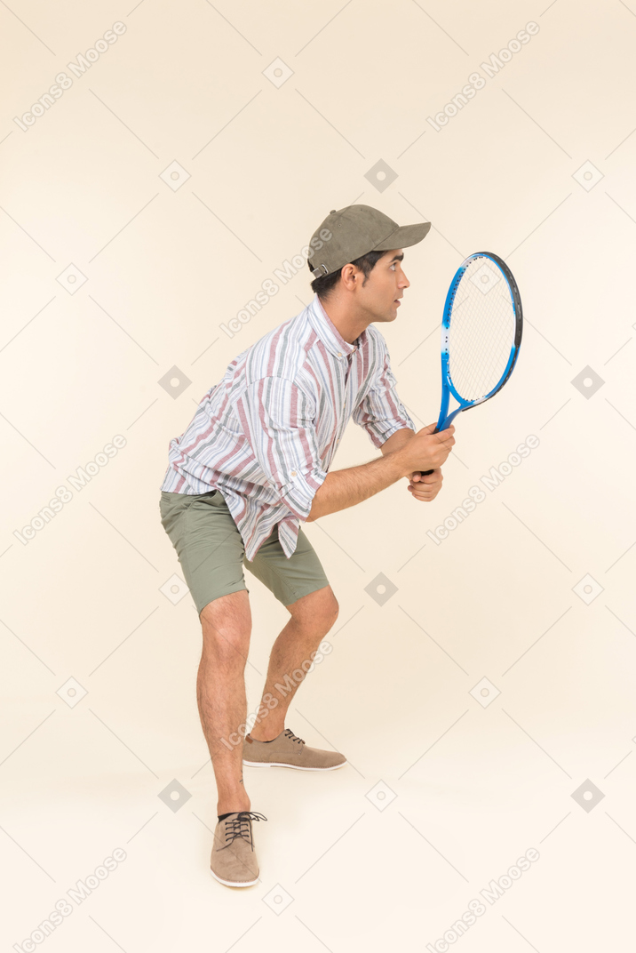 Young caucasian man standing half sideways and holding tennis racket
