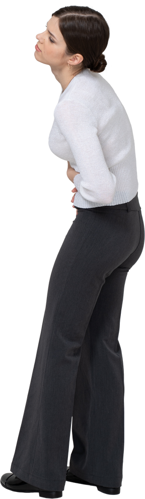 Vista posterior de tres cuartos de una mujer joven en ropa de oficina tocando el estómago