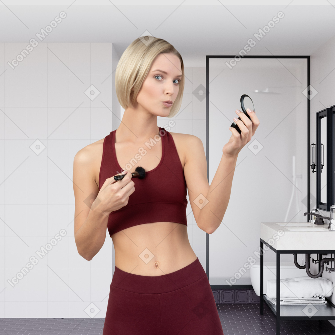 Mujer joven parada en el baño y maquillándose