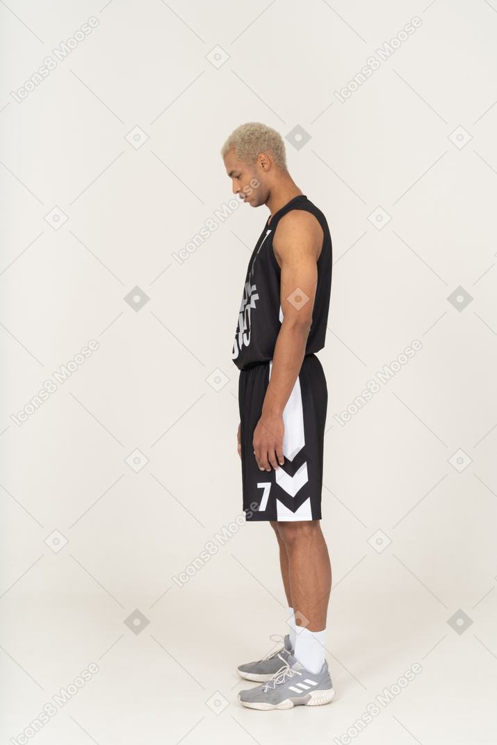 Vista laterale di un giovane giocatore di basket maschile in piedi immobile e guardando in basso