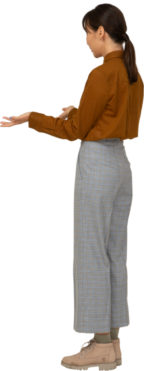 Three-quarter back view of a questioning young asian female in breeches and blouse raising hands