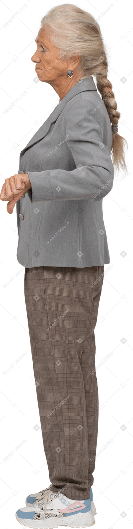 Vista lateral de una anciana molesta en traje mostrando el pulgar hacia abajo