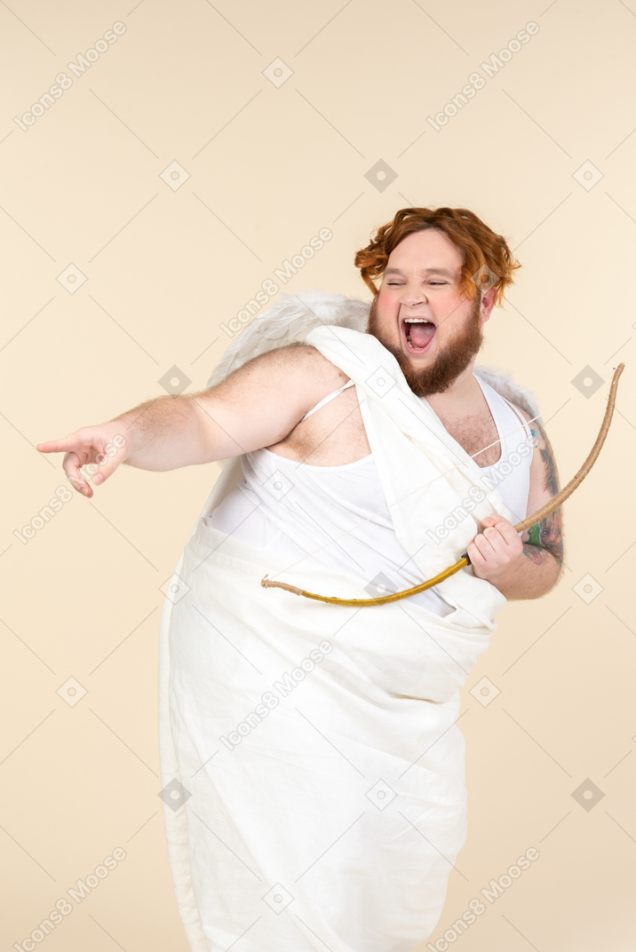 Un joven riendo vestido como un cupido sosteniendo un arco y señalando