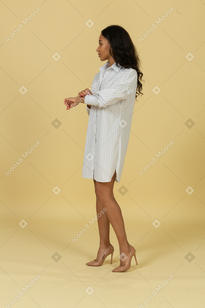 Vista di tre quarti di una giovane donna dalla carnagione scura in abito bianco che si abbottona la manica