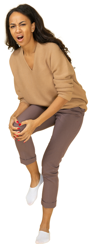 Vista de tres cuartos de una joven de piel oscura tocando su rodilla herida