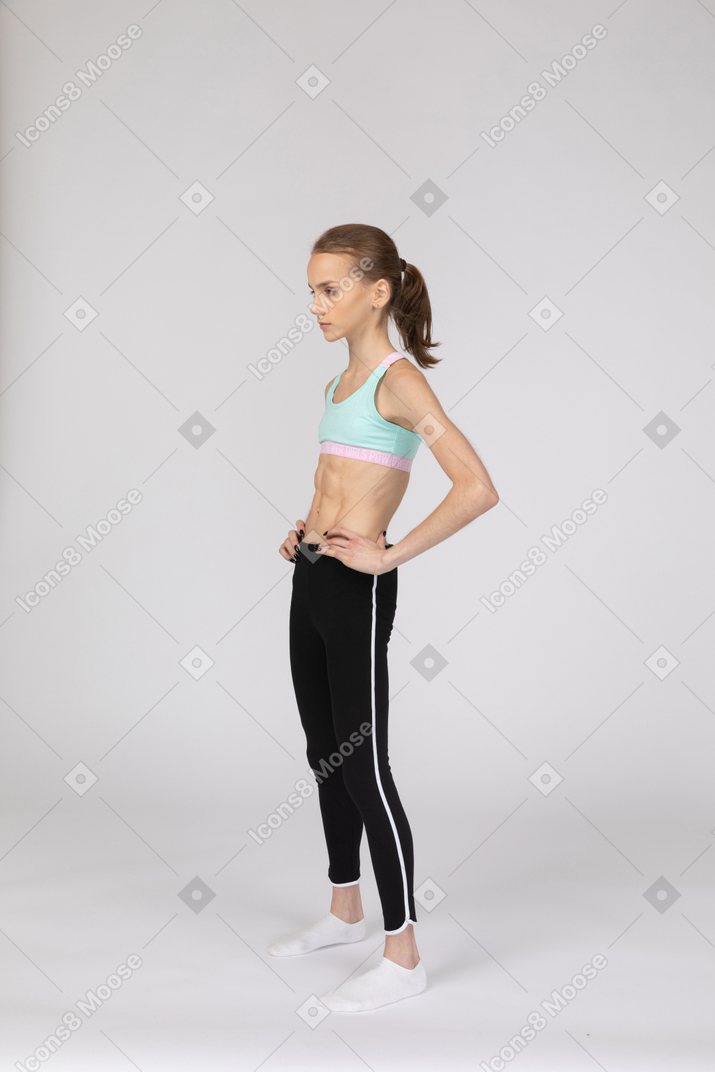 Vista de três quartos de uma adolescente em roupas esportivas colocando as mãos nos quadris