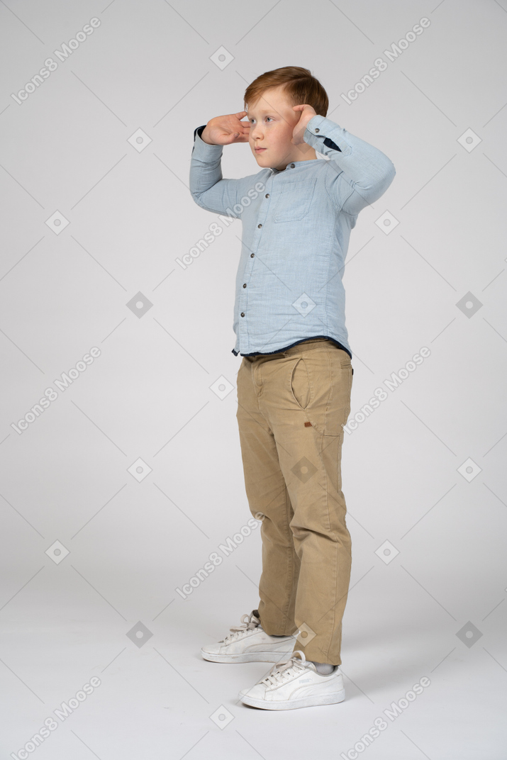 Vista lateral de un niño posando con las manos en la cabeza