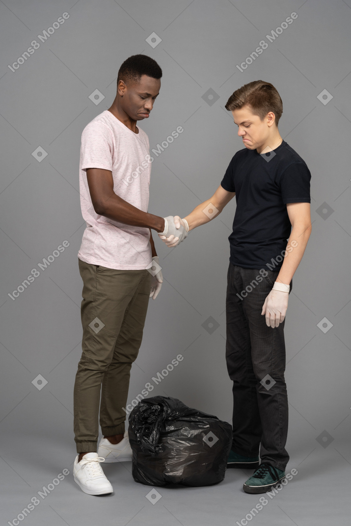 Two friends shaking hands above a trash bag