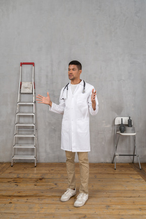 Vue de trois quarts d'un jeune médecin gesticulant debout dans une pièce avec échelle et chaise
