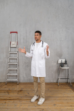 Vista de tres cuartos de un joven médico gesticulante de pie en una habitación con escalera y silla