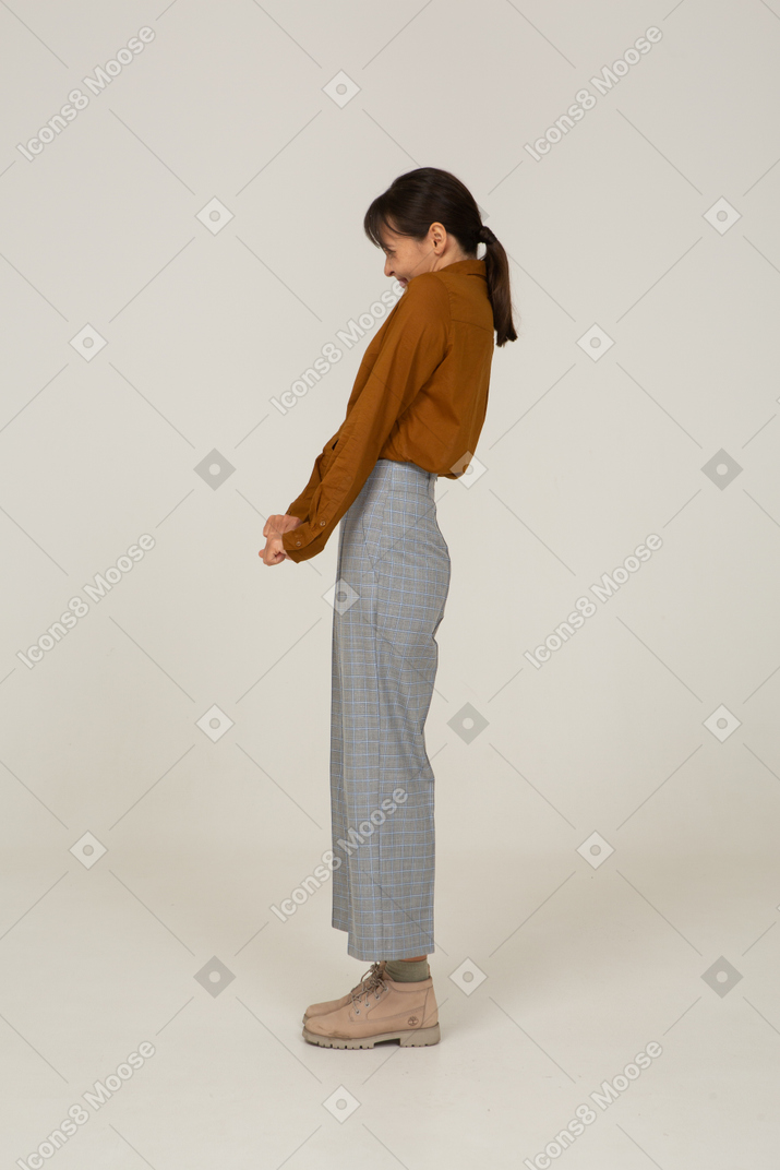 Vista laterale di una giovane donna asiatica in calzoni e camicetta che si tiene per mano e si appoggia all'indietro