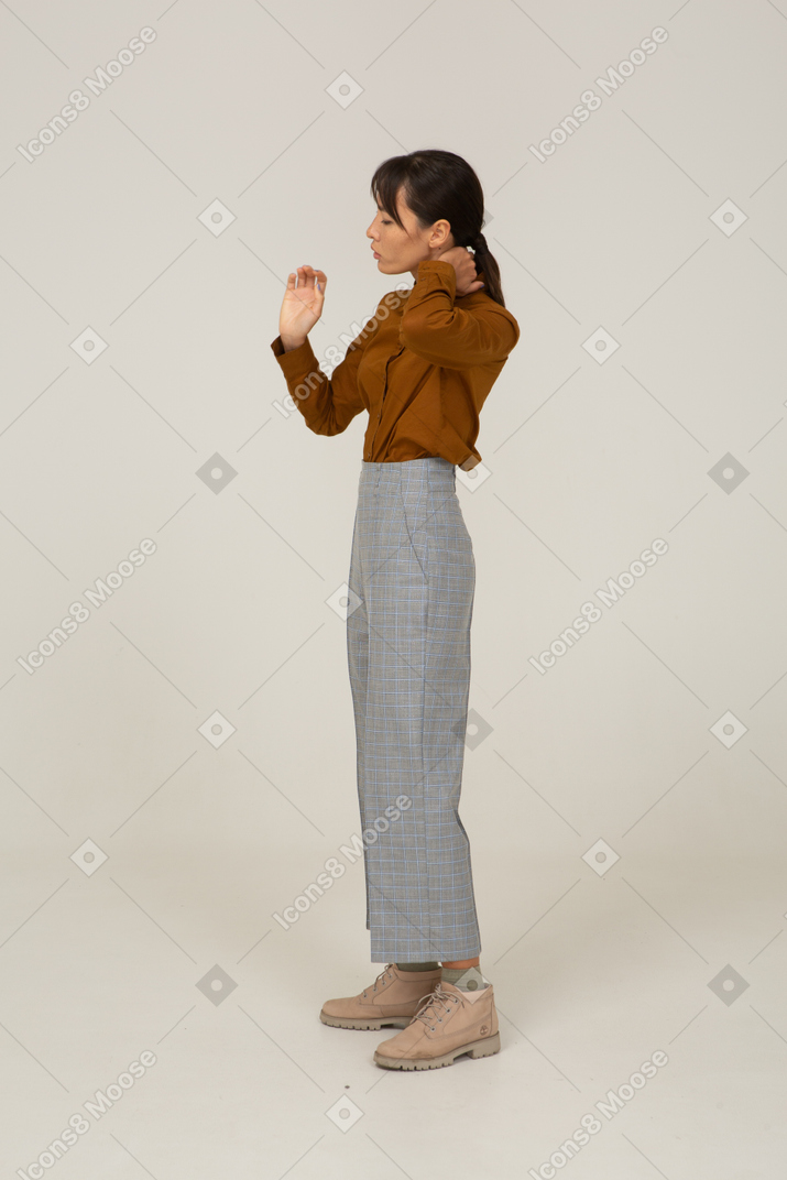 Side view of a young asian female in breeches and blouse touching neck