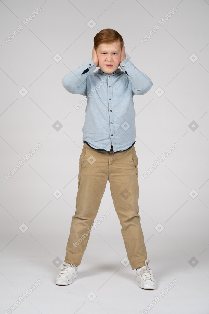 一个愤怒的男孩用手捂住耳朵，看着相机的正面图