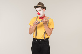 Male clown using knife as nail file