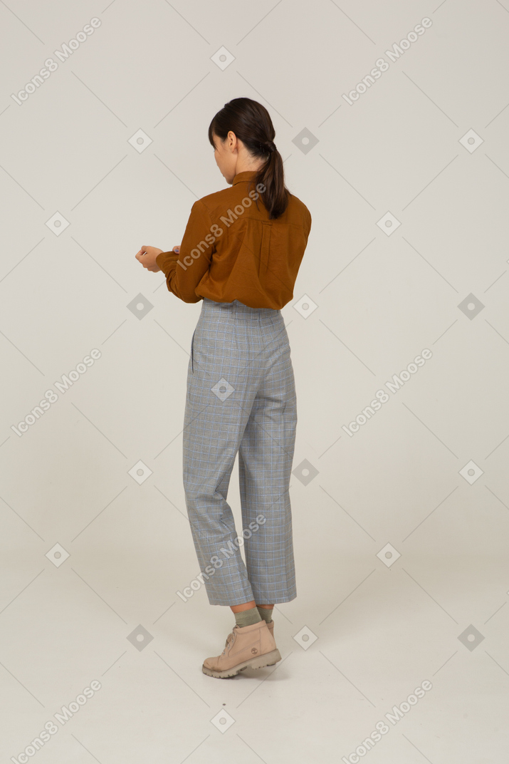 Vue de trois quarts arrière d'une jeune femme asiatique en culotte et chemisier boutonnant sa manchette